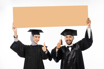 Wall Mural - Couple of graduate student wearing toga holding cardboard blank space on isolated background