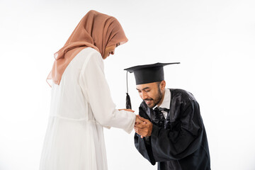 Wall Mural - Graduate male student wearing toga shaking hands kissing mother's hand on isolated background
