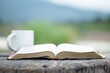 Open the bible with a cup of coffee for morning devotion on a wooden table with nature background.