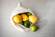 Fresh lemons and limes in a fabric bag on a light stone background. Top view