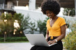 © fotofabrika - Young african american woman working on laptop sitting on the bench at the city
