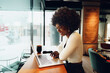 © fotofabrika - Smiling young african woman sitting with laptop in cafe