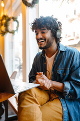 Wall Mural - Young smiling handsome indian curly man holding videoconference with laptop