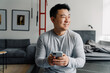 Brunette adult asian man smiling and using cellphone at home