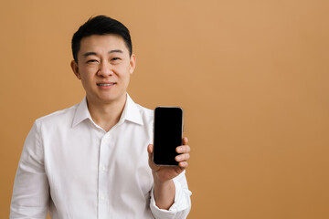 Wall Mural - Brunette adult asian man smiling and showing cellphone at camera