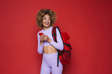 Wall Mural - Young black woman with backpack smiling and holding cellphone