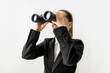 Smiling business woman in jacket looking through binoculars on white background