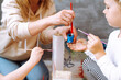 © Татьяна Волкова - Cropped photo of young woman teacher showing how to stir blue gouache with red brush in plastic jar to little girl.