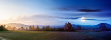 Panorama Of A Carpathian Rural Landscape At Twilight. Arable In Front Of A Forest In Colorful Foliage. Day And Night Time Change Concept. Distant Mountains Beneath A Sun And Moon. Hazy Atmosphere
