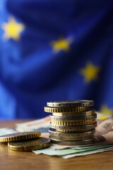 Coins and banknotes on wooden table against European Union flag, space for text