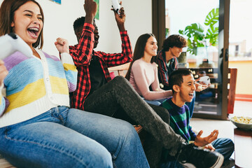 Multiracial young friends having fun playing video games at home - Focus on left african guy arm