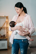 © PR Image Factory - portrait affectionate asian mother is gazing at her infant child in arms while breastfeeding in a standing position at home.