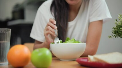 Wall Mural - Hand of Young female eating organic green vegetable salad in weight loss diet and wellness on table. Beautiful woman happily eat a healthy salad breakfast in kitchen in the morning. Diet food concept.