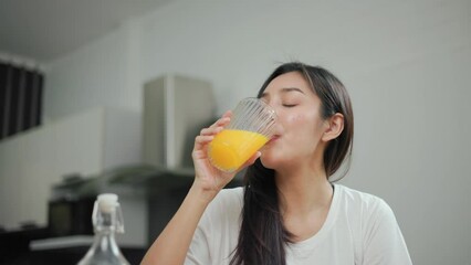 Wall Mural - Young female drinking organic orange juice in weight loss diet and wellness on table. Beautiful woman happily drink a healthy fruit juice breakfast in kitchen in the morning. Vitamin c food concept.