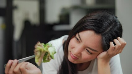 Wall Mural - Unhappy female looking to organic greens vegetable salad in weight loss diet and wellness on table. Tired woman dislike eat bored with food healthy salad breakfast in kitchen. Diet food concept.