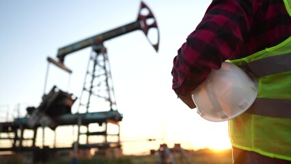 oil production. a worker holding a protective hard hat at sunset in the background an oil pump. oilfield business a extraction concept lifestyle. oil extraction pump. oil pump rig