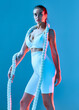 © Georgii - A beautiful brunette lady of athletic build stands with a rope on her shoulders. The girl is dressed in white sportswear on a blue background.