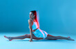 © Georgii - Athletic girl is sitting on the splits. A brunette woman in white uniform on blue background.