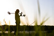 © Nyaaka - The silhouette of a young man with a wireless metal detector looks ahead.  On the bank of the river, in the foreground the grass is in blur