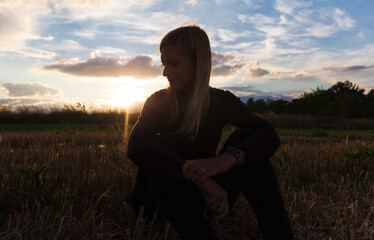 Silhouette of sitting young blonde caucasian woman with sunset dramatic sky