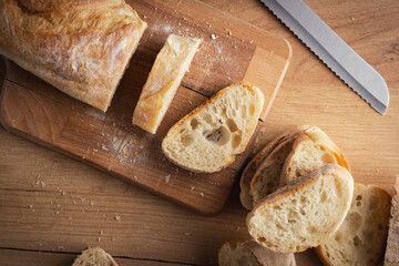 Wall Mural - Whole grain bread close-up on the wooden cutting board. Knife with serrated blade. Fresh bread on the wooden kitchen table. Flat lay with traditional pastries in bakery