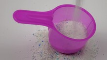 Pouring detergent powder into a pink plastic measuring scoop for laundry powder on a white background