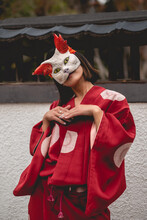 Portrait Of Sexy And Young Japanese Girl With Beautiful Old Traditional Red Kimono And Handmade Cat Mask Dancing In Front Of A Old White Wall In A Japanese Garden