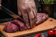 the chef cuts a piece of veal beef meat on a dark background, Whole piece of tenderloin with steaks and spices ready to cook