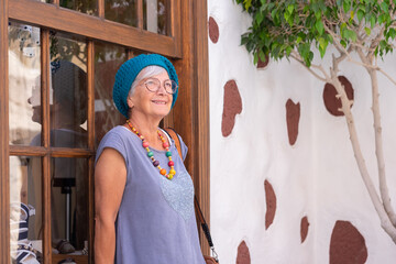 Sticker - Beautiful senior woman standing out of a shop window smiling and looking away