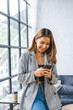 © Phushutter - Young pretty Asian woman using mobile phone in living room near windows.