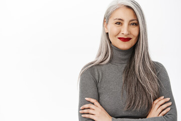 Close up portrait of stylish, healthy and beautiful asian middle-aged woman, smiling, looking confident and happy, standing in professional power pose, white background