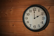 An old black and white wall clock hanging on a wooden wall shows two a clock.