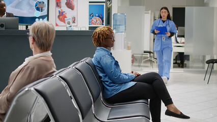 Asian nurse taking african american woman to do checkup visit with doctor in medical office. Female patient waiting in hospital reception lobby to start consultation appointment.