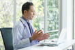 © aekkorn - Asian senior doctor sitting in medical office while video call meeting using laptop computer.