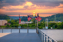 American Flags Flying On The Edge Of The Pier Surrounded By The Flowing Waters Of The Tennessee River And Lush Green Trees With Blue Sky And Powerful Clouds At Sunset At Ross's Landing In Chattanooga