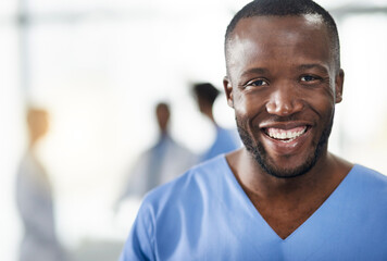 Poster - Happy, smiling and professional doctor in a hospital closeup portrait with blurred background. Confident black male medical healthcare worker with colleagues in the back. An African American surgeon.