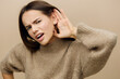 © Tatiana - a funny, emotional, upset woman holds her hand near her ear, listening with her mouth wide open and looks with a puzzled expression on her face. Close horizontal, studio photography