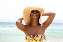 Beautiful black woman standing at the seashore wearing a sun hat on the beach and relaxing
