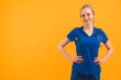 © PoppyPix - Young blonde white female nurse wearing ponytail and scrubs standing with hands on hips smiling looking into camera. Studio shot. High quality photo