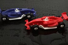 Two Racing Cars In Blue And Red Stands On A Dark Background.