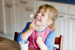 © Irina Schmidt - Little toddler girl eating yogurt for breakfast. Cute healthy baby sitting in the kitchen or at nursery and having meal.