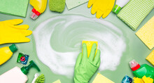 Home cleaning products. A hand in a green rubber glove wipes soap suds with a washcloth on a green background. Concept of cleanliness, cleaning services.