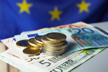 Coins and banknotes on table against European Union flag, closeup