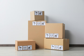 Canvas Print - Many closed cardboard boxes with packaging symbols on floor near white wall. Delivery service