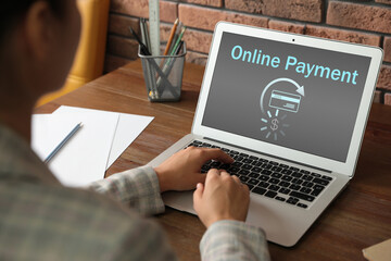 Woman using laptop for online payment at wooden table, closeup