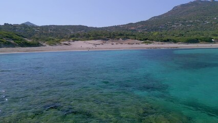 Wall Mural - Aerial view pulling back across the translucent water of the Mediterranean sea away from the sandy beach of Bodri in the Balagne region of Corsica