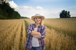 © olga_sova - A beautiful middle-aged farmer woman in a straw hat and a plaid shirt stands in a field of golden ripening wheat during the daytime in the sunlight