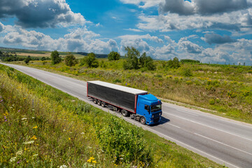 Wall Mural - blue cargo truck on the highway. asphalt road among green fields and beautiful clouds. cargo delivery and transportation concept