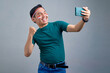 © Bangun Stock Photo - Excited young Asian man in casual t-shirt streaming online video on mobile phone, celebrating victory isolated on grey background. indonesian independence day celebration concept