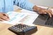 © Sai - Businessman using calculators and laptops to calculate financial figures working in the office. Financial accounting concept